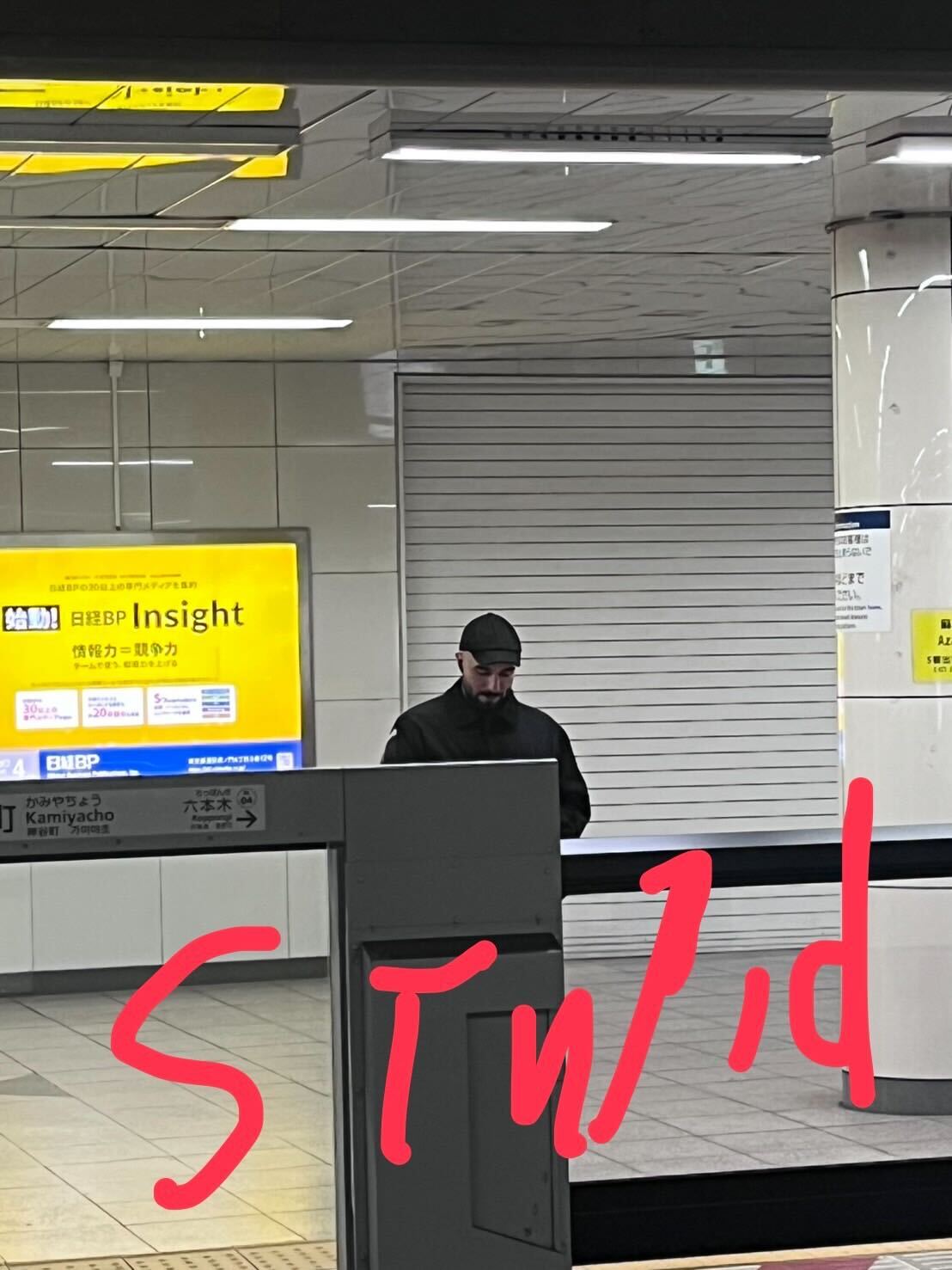 Vic standing in the train station. A handwritten note over the picture reads: 'Stupid'